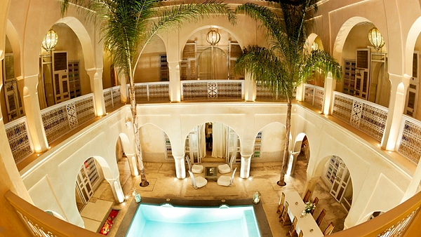 Patio de un riad de lujo visto desde arriba: arcos, palmeras, faroles y piscina iluminada