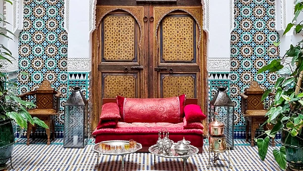 Salón de un riad tradicional: banco de terciopelo rojo, puerta de cedro tallado, paredes de zellige y servicio de té de plata