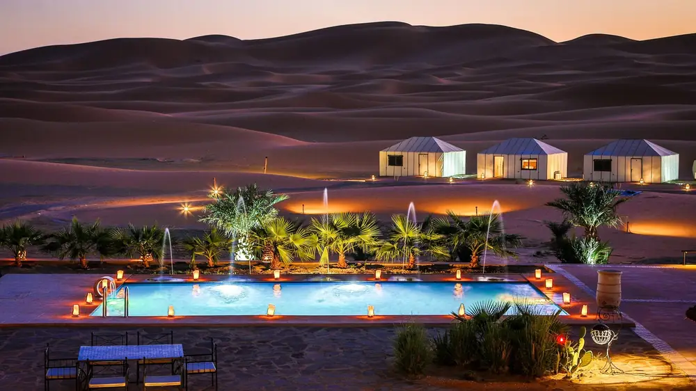 Campamento de lujo y su piscina iluminados al pie de las dunas