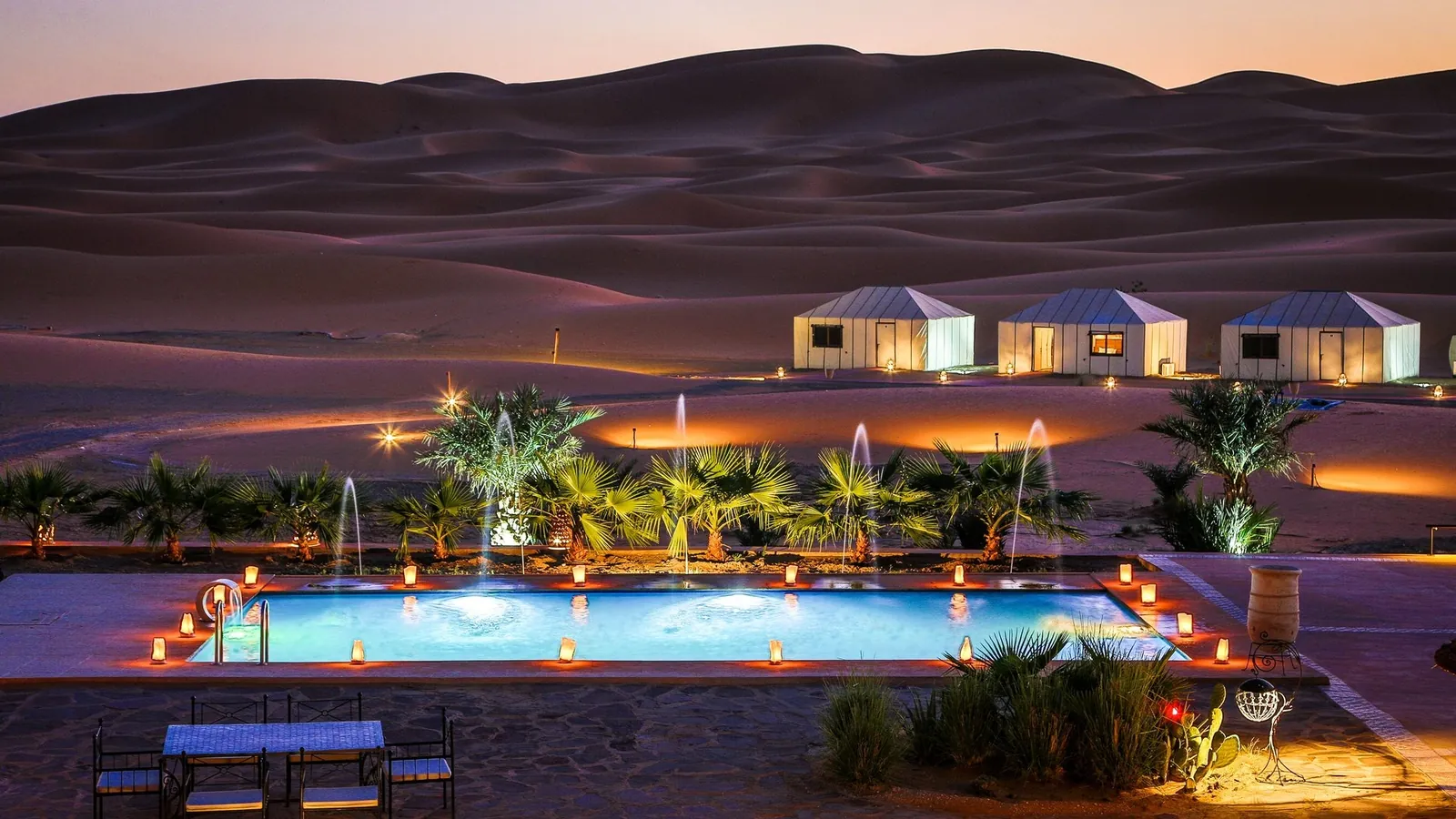 Campamento de lujo y su piscina iluminados al pie de las dunas