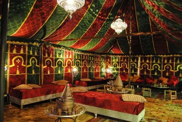 Interior de una jaima caidal con alfombras rojas y farolillos